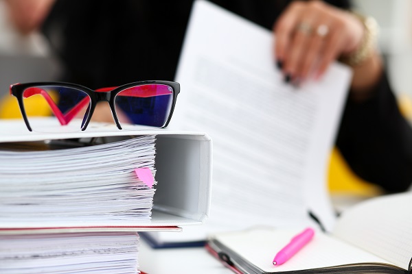 Person going through legal investigation document paperwork with glasses on top of folders